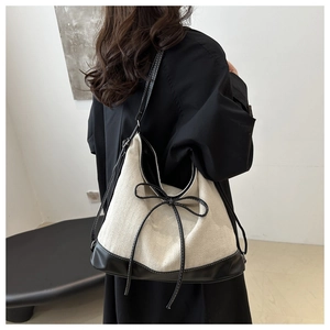 Detail of canvas tote bag showing black leather trim and woven bow decoration on shoulder