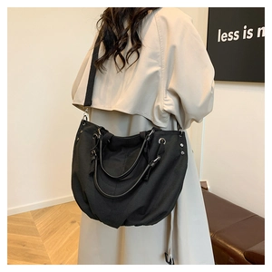 Detail of black canvas tote bag with leather handles and metal rivets on beige trench coat