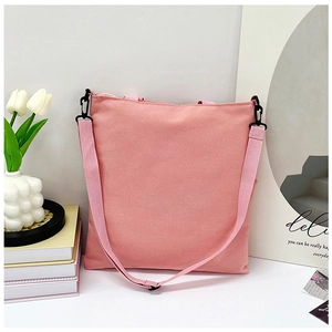 Detail of pink canvas tote bag with black hook buckle and strap in a minimalist setting