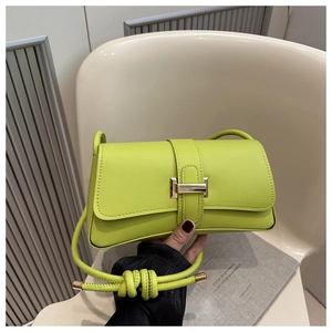 Close-up of lime green leather handbag featuring a gold H-shaped clasp on an armchair