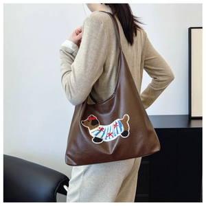 Dettaglio di una borsa tote marrone con ricamo a forma di bassotto indossata a spalla