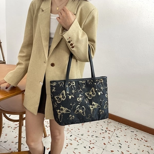 Large black jacquard tote bag with golden butterfly pattern worn on the shoulder