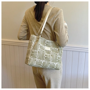 Detail of olive green striped canvas tote bag worn on shoulder over minimalist background