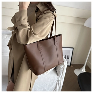 Close-up of a large brown leather tote bag styled with a khaki trench coat for commuting