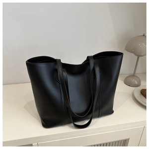 Detail of a large black faux leather tote bag with reinforced handles in a home setting