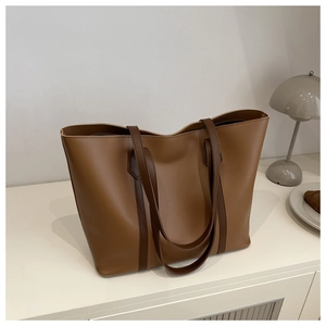 Caramel leather tote bag on minimalist desk with croissant and lamp in soft lighting