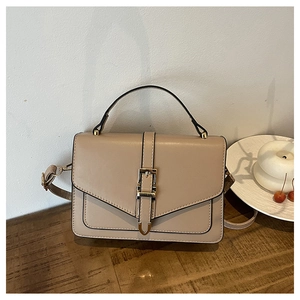 Minimalist beige crossbody bag with metal buckle closure on a rustic wooden table