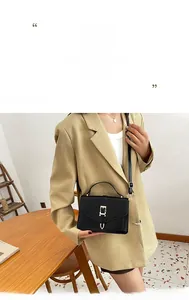 Detail of a chic black leather crossbody bag with metal buckle on a khaki blazer