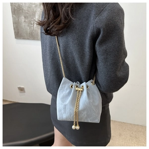 Detail of light blue bucket bag featuring gold chain strap and pearl drawstring tassels