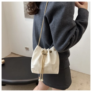 Close-up of cream drawstring bucket bag with gold chain strap and pearl charms