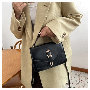 Detail of a vintage black leather crossbody bag with a prominent golden buckle