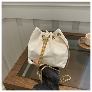 Detail of white drawstring bucket bag with gold chain and pearl accents on a wooden table