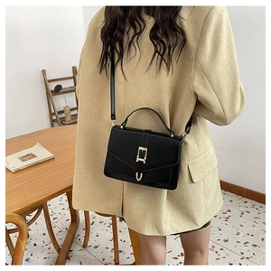 Detail of a chic black leather crossbody bag with a gold buckle worn with a yellow blazer