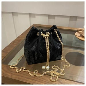 Detail of black velvet bucket bag featuring gold chain and white pearl drawstring toggle