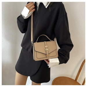 Classic camel crossbody bag with gold buckle detail shown on a model in a minimal setting