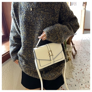 Close-up of a white leather crossbody bag with gold buckle and black piped edges