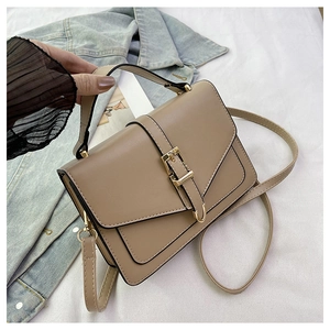 Detail view of khaki square crossbody bag with metal buckle on denim jacket background