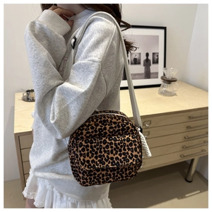 Detailed view of leopard print canvas crossbody bag worn by model in a cozy setting