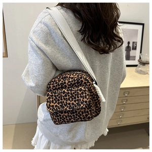 Close-up of leopard print crossbody bag with white woven strap in casual indoor setting