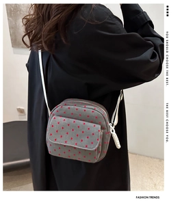 Detail of grey crossbody bag with red heart polka dots and white woven strap