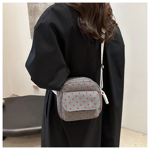 Detail of grey crossbody bag featuring red heart embroidery and white stitching accents