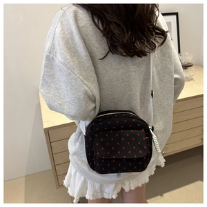 Vue détaillée du sac bandoulière en toile noire à motifs cœurs rouges sur un sweat gris