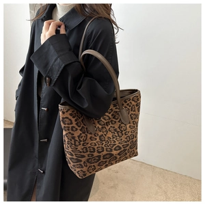 Model wearing a large leopard print tote bag with brown leather handles in a side view style
