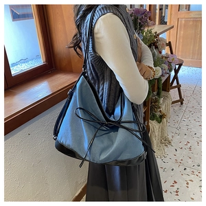 Detail of blue denim tote bag with leather straps and decorative bow tie on a model