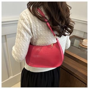 Sac à bandoulière en cuir verni rose fuchsia porté par un mannequin élégant