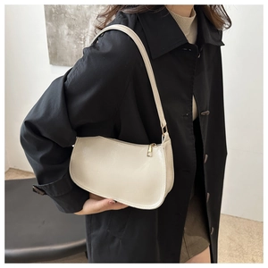 Close-up of a cream white minimalist shoulder bag with gold zipper on a black coat