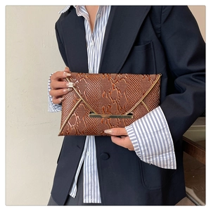 Detail of dark brown snake-embossed leather envelope clutch with gold metal trim and flap