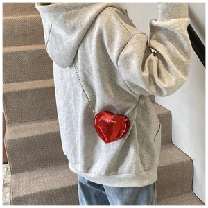 Red heart-shaped patent leather crossbody bag with silver chain strap shown on model