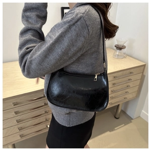 Détail du sac sous le bras en similicuir noir brillant avec fermeture éclair dorée