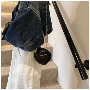 Detail of a shiny heart-shaped black crossbody bag with chain strap and text