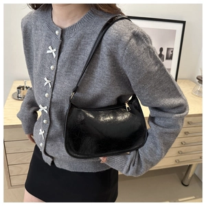 Glossy black patent leather underarm bag with gold zipper shown on model in home setting