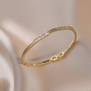 Elegant gold bangle with zircon inlay displayed on luxury champagne silk fabric