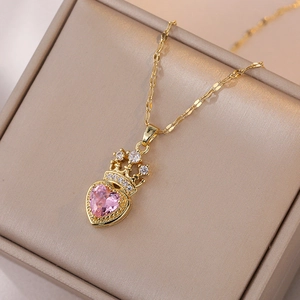 Collier couronne dorée avec pendentif cœur en cristal rose sur une boîte à bijoux en satin