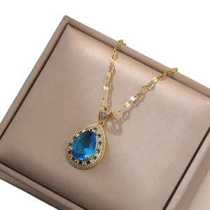 Collana a goccia d'oro con gemma blu e halo di diamanti verdi su scatola portaoggetti