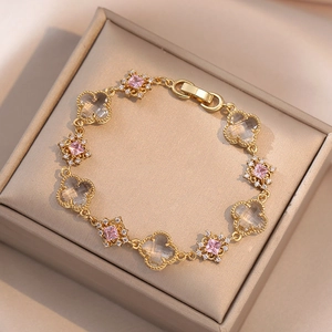 Macro shot of gold-plated chain bracelet with emerald-cut pink stones and clover charms