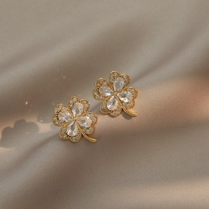 Elegant gold four-leaf clover stud earrings with sparkling crystals on champagne silk