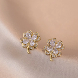 Elegant gold four-leaf clover stud earrings with sparkling crystals on champagne silk