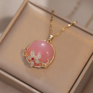 Collier avec pendentif pierre rose et décorations florales dorées sur boîte à bijoux