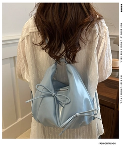 Detail of light blue glossy shoulder bag with bow knot on a model in a cozy interior