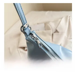 Detail shot of smooth silver zipper and metallic ring hardware on light blue shoulder bag