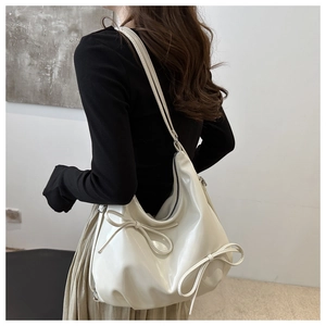 Detail showing side bow design and glossy leather texture of the creamy white tote bag