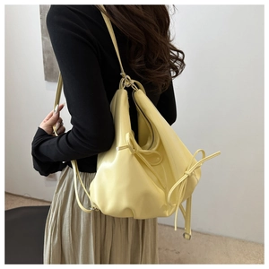 Detail of light yellow ruched cloud bag with bow tassels on shoulder of a model