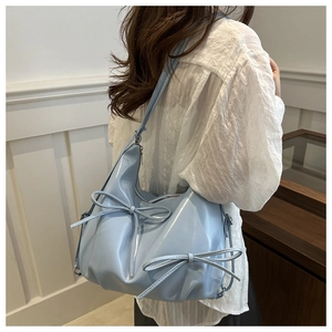 Detail of light blue glossy leather shoulder bag with decorative bows on a model