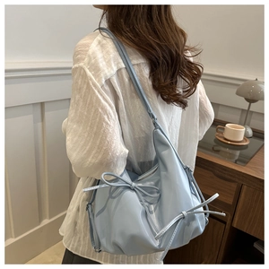 Detail of light blue patent leather shoulder bag with decorative bow ties and silver zipper