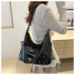 Detail of black glossy tote bag featuring side bow accents and silver zipper closure