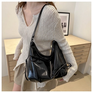 Close-up of black glossy hobo bag with delicate ribbon bows on minimalist wooden background